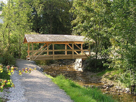 Holzbrücke aus gefrästem Rundholz mit Schindeldach
